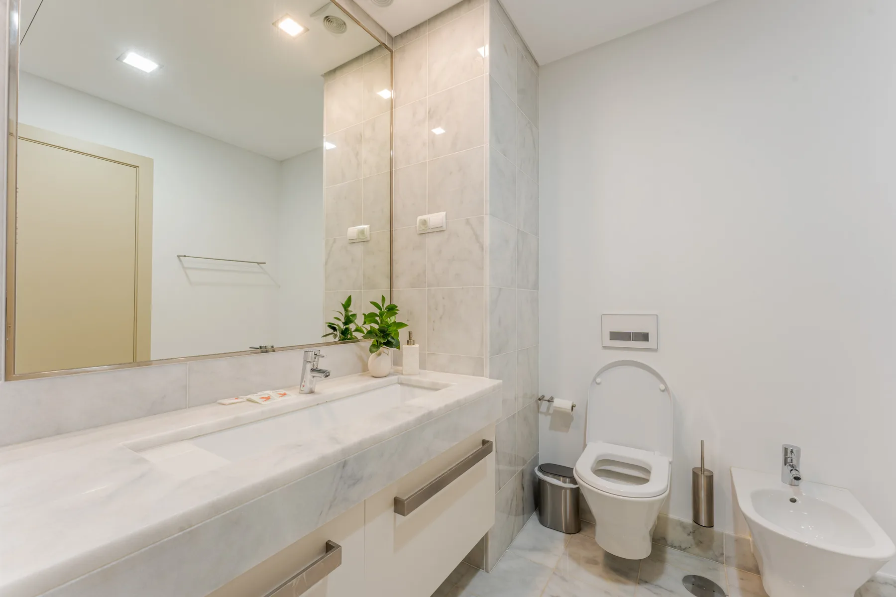 A bright bathroom with a long vanity, toilet, and bidet.