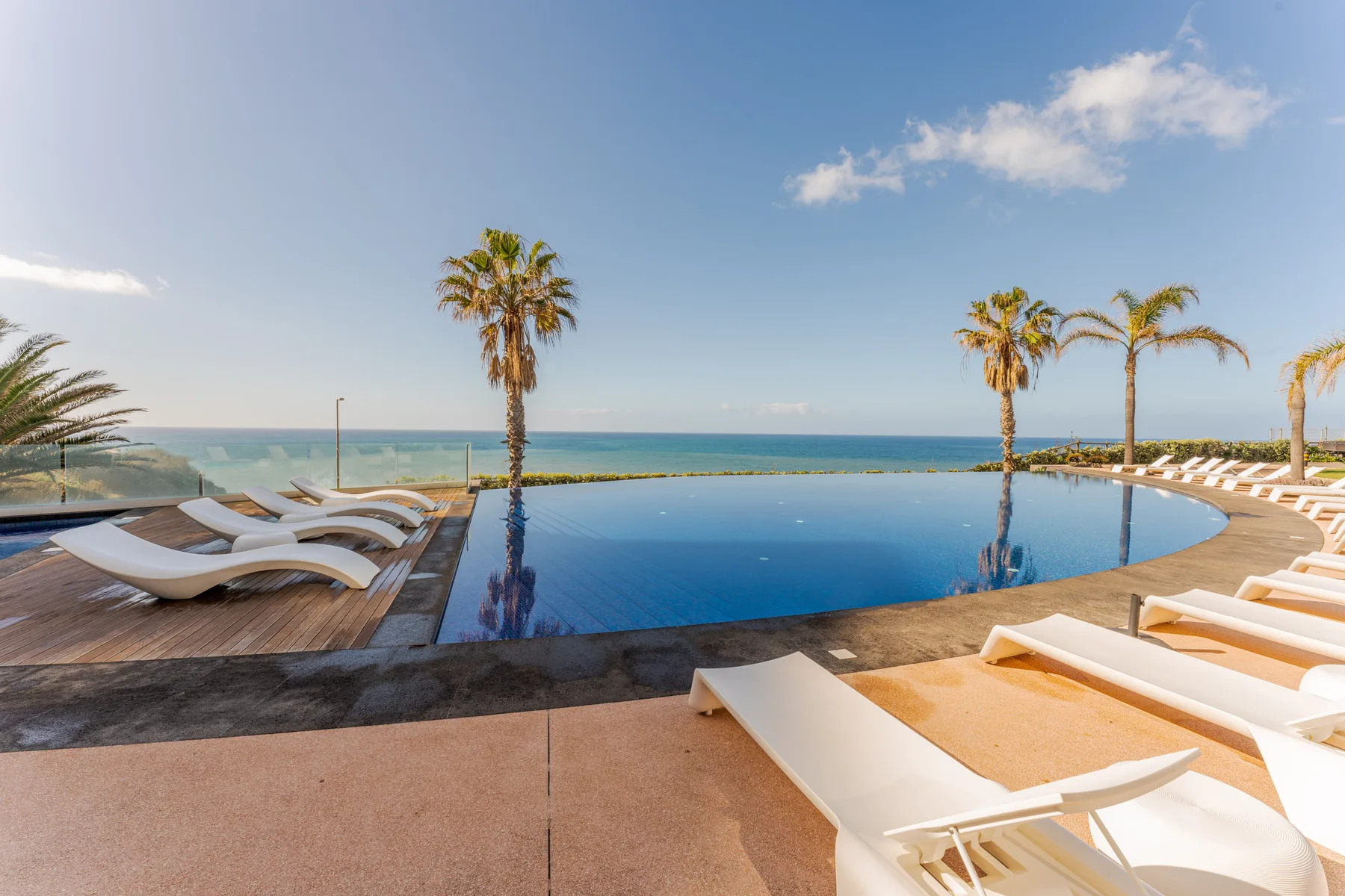 An outdoor swimming pool overlooks the ocean, with lounge seating around its edge.