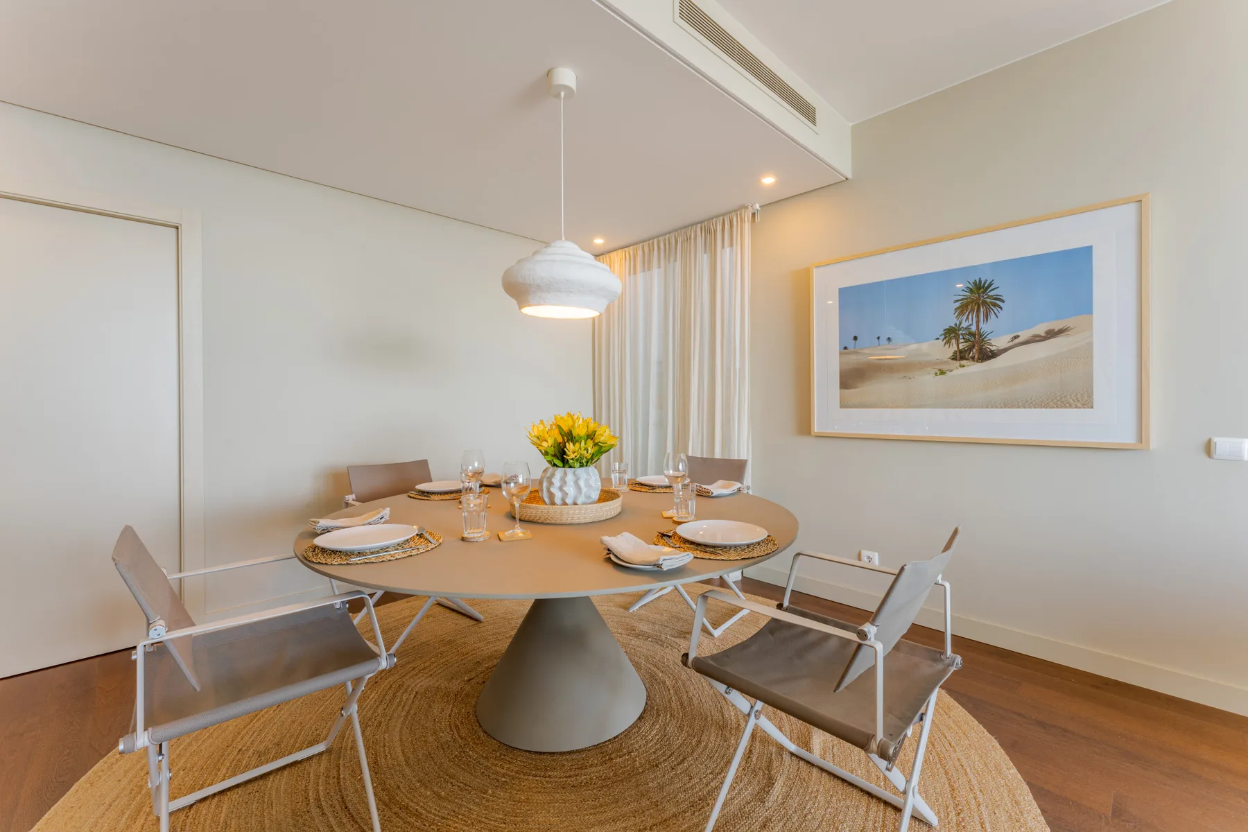 A dining area with a round table, set for a meal beside a framed beach print.