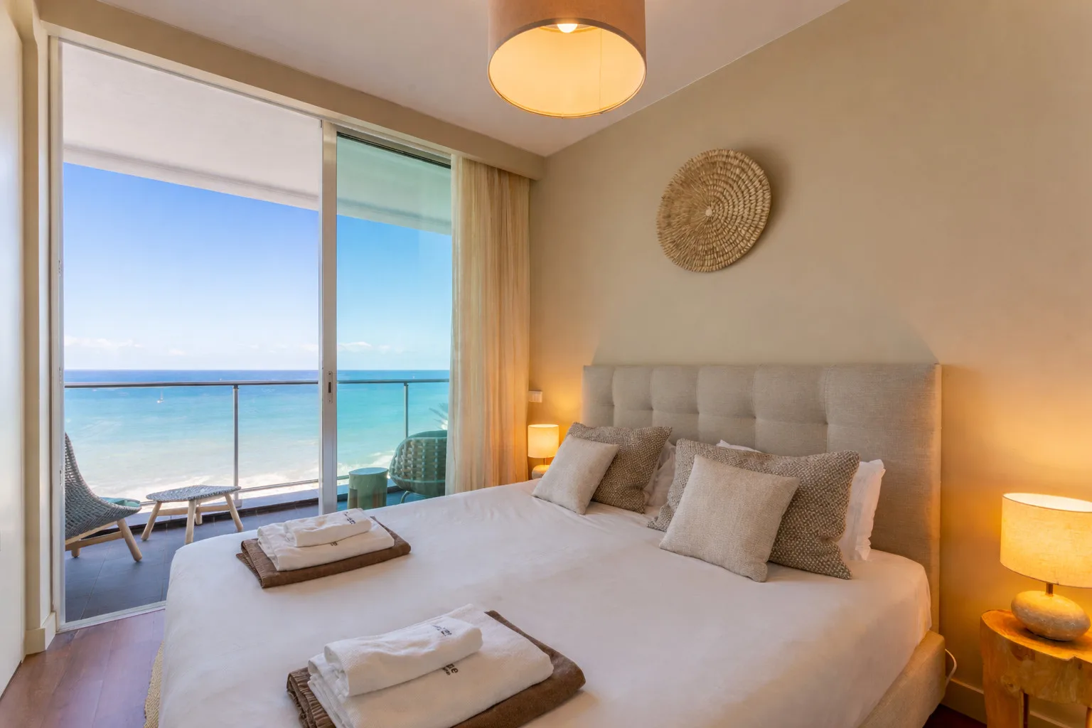 A bedroom with a large bed and sliding glass doors opening onto a sea view.