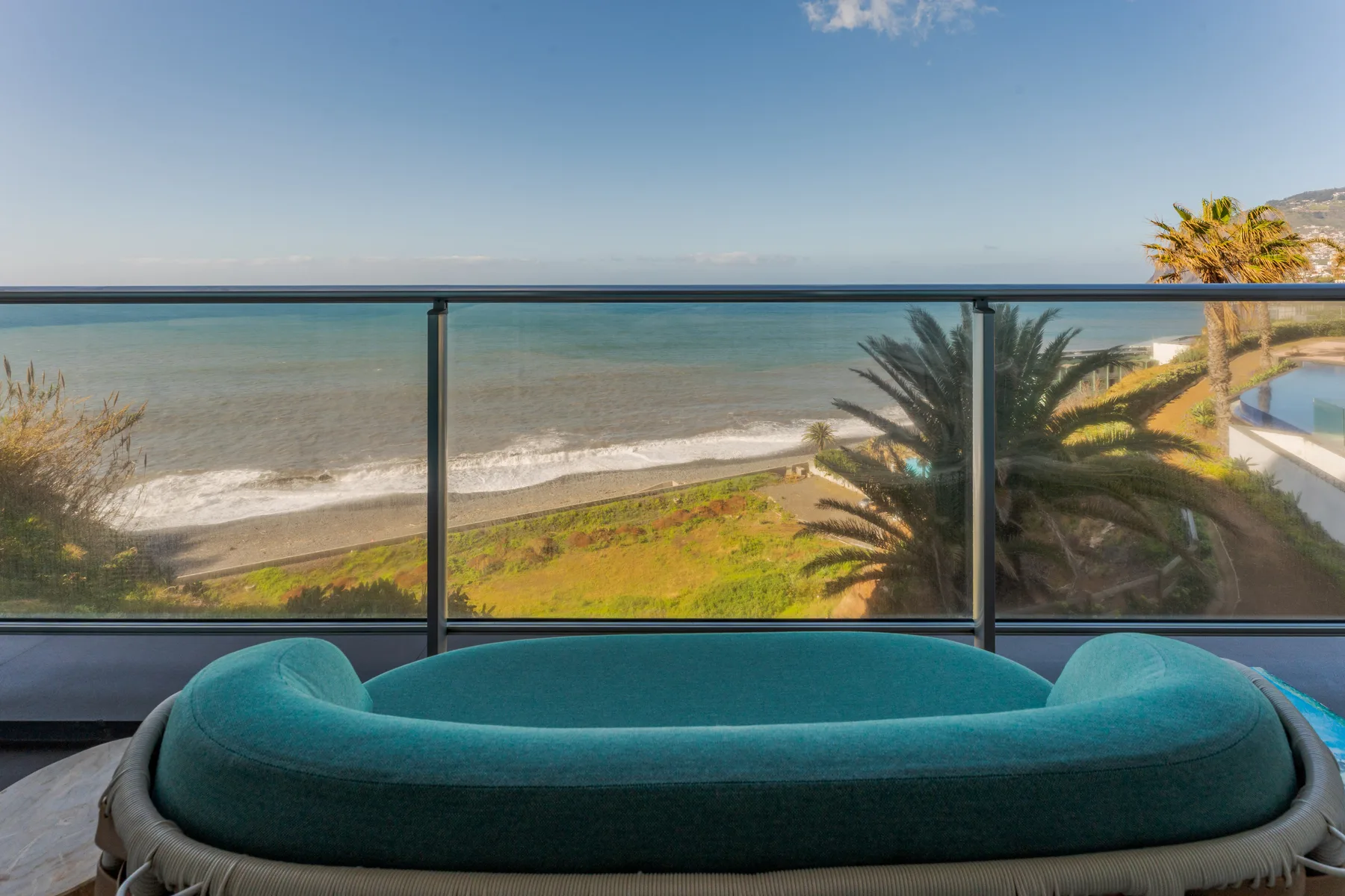 A turquoise outdoor seating area overlooks the ocean from a glass-railed terrace.