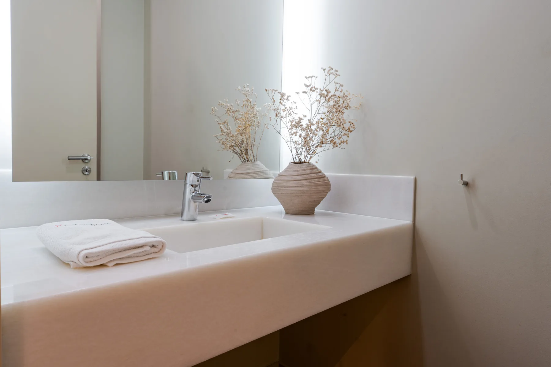 A bright bathroom vanity with a sink, mirror, and dried flowers.
