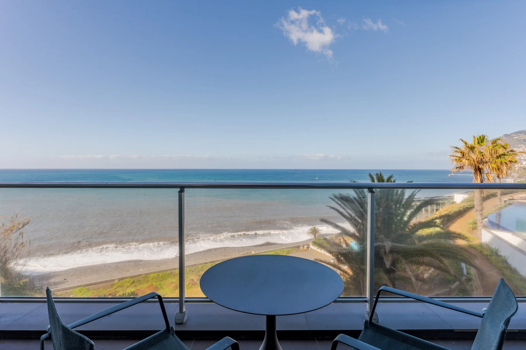 A balcony seating area overlooks the ocean and a sandy beach.