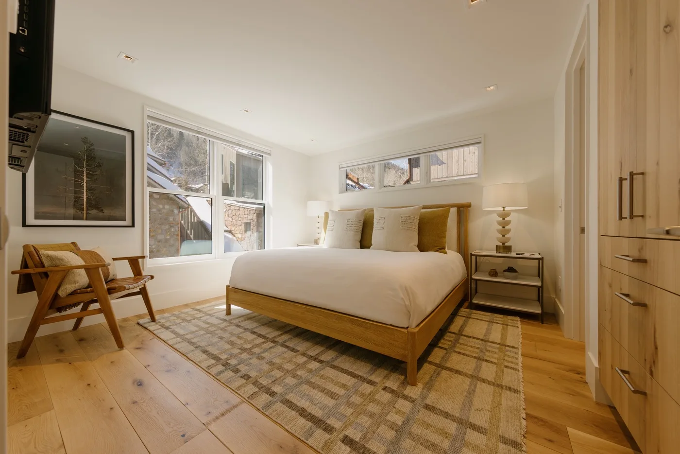 Un dormitorio luminoso con una cama grande y ventanas con vistas a los edificios cercanos.