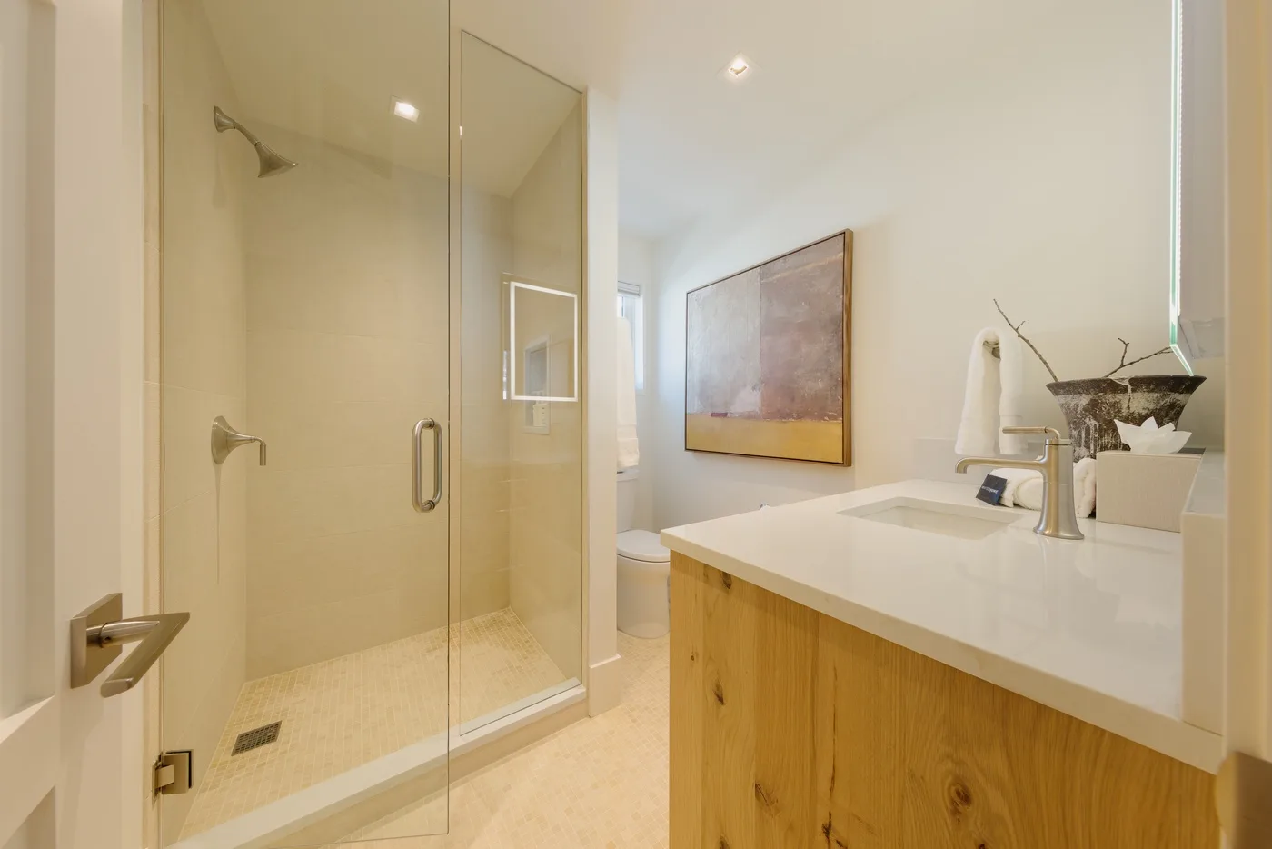 Un baño luminoso con una ducha de vidrio y un mueble de lavabo de madera.