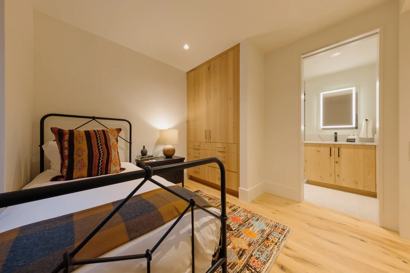 Un dormitorio con una cama de metal, armarios de madera y una puerta abierta hacia un tocador.
