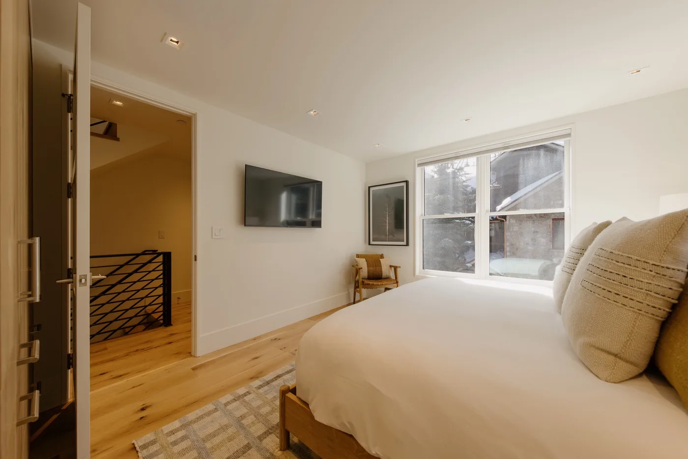 Un dormitorio con una cama, un televisor montado en la pared y una ventana grande.