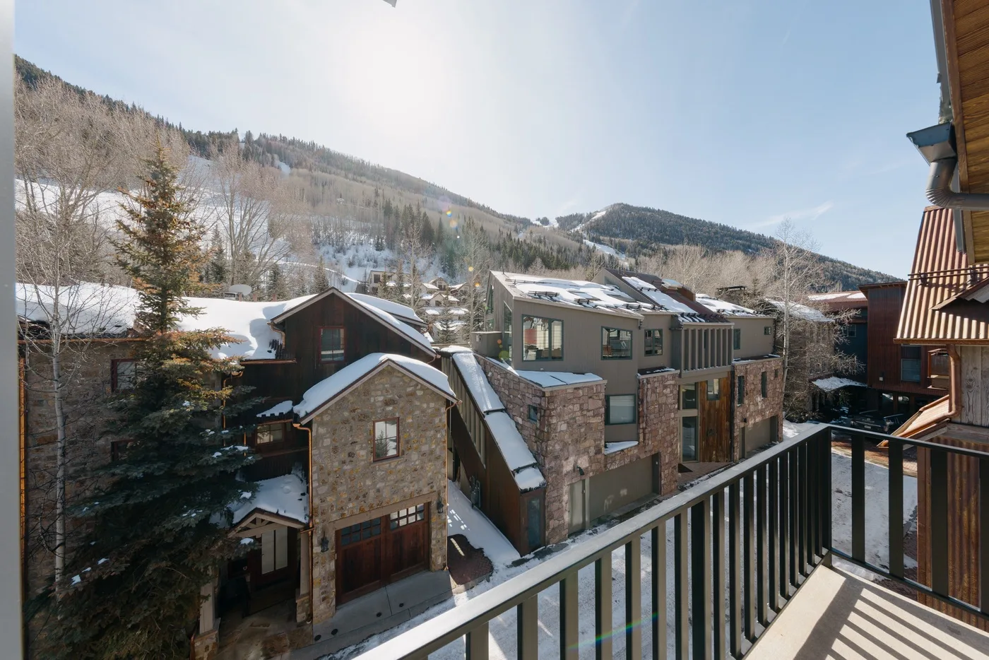 Edificios cubiertos de nieve se encuentran bajo colinas boscosas, vistos desde un balcón.