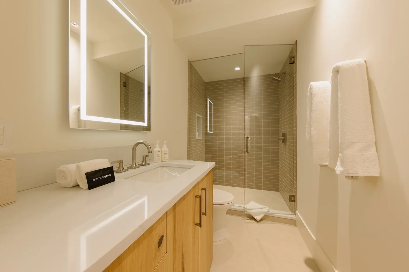 Un baño luminoso con un tocador largo, espejo iluminado y ducha de vidrio.