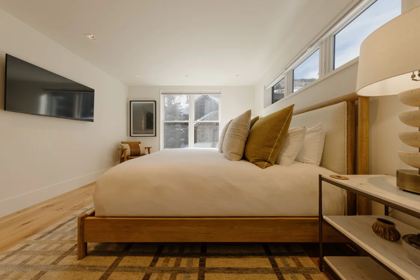Un dormitorio luminoso con una cama grande y un televisor montado en la pared.