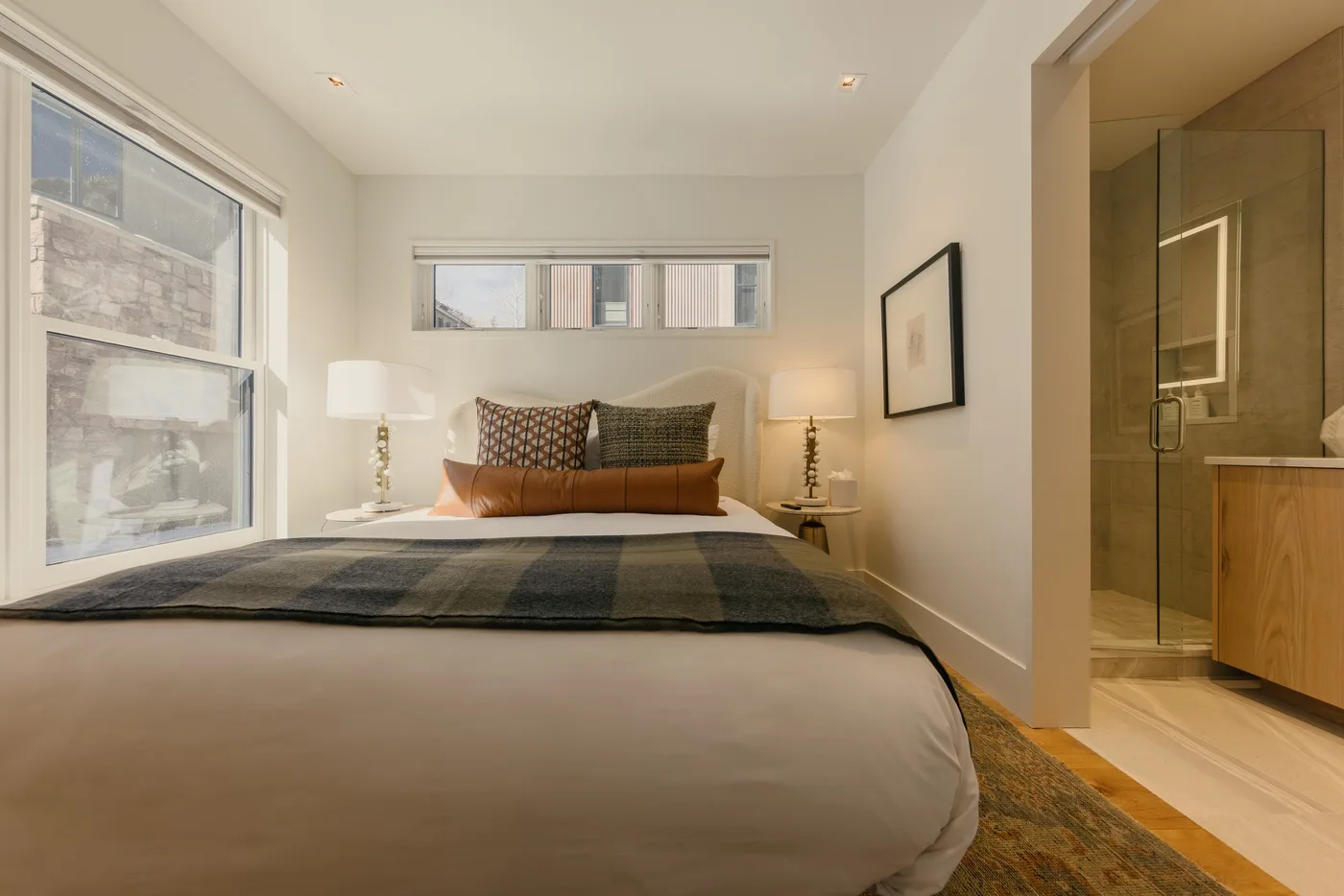 Un dormitorio con una cama bajo una ventana amplia y una ducha contigua.