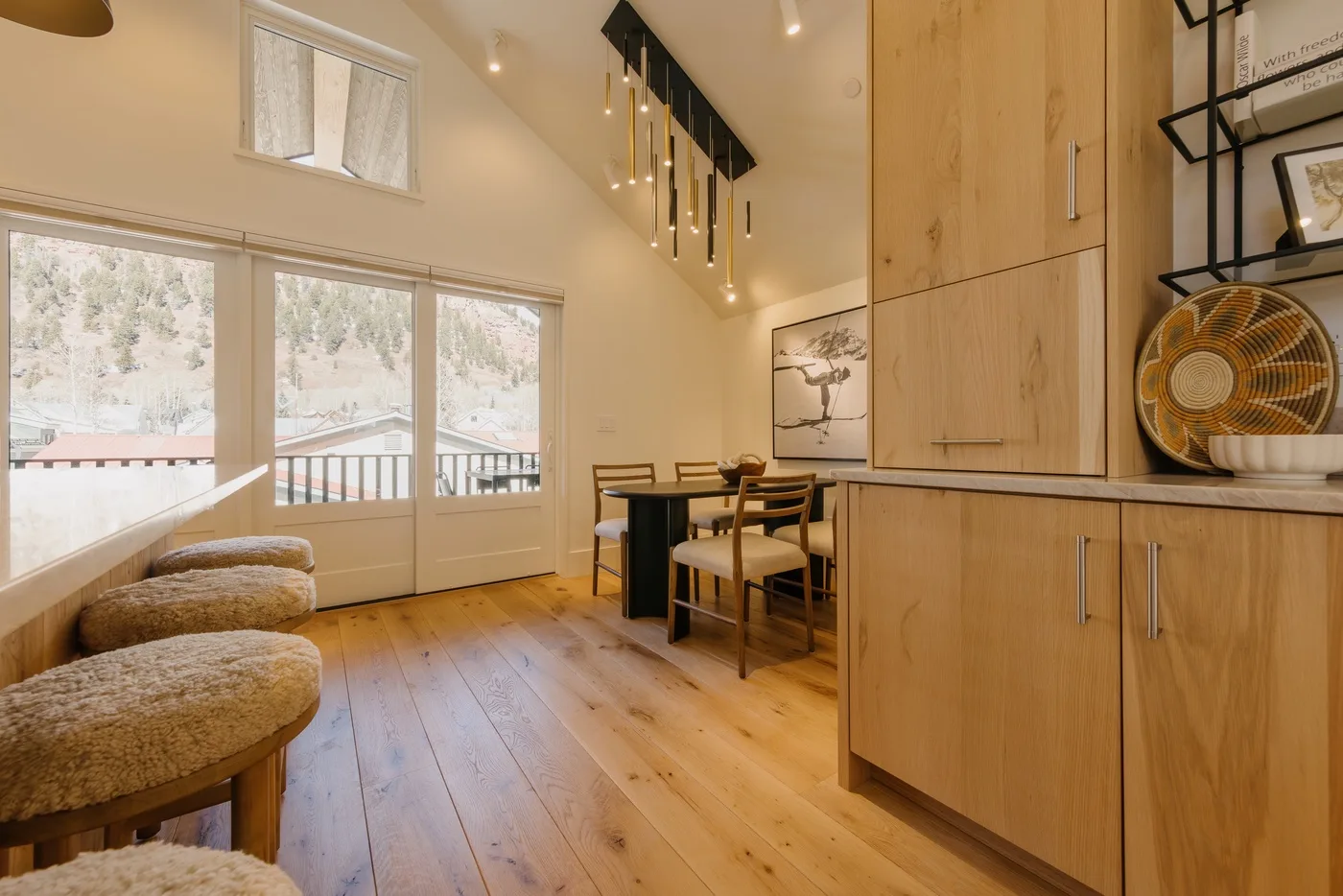 Comedor con mesa y sillas junto a grandes ventanas y gabinetes de madera.