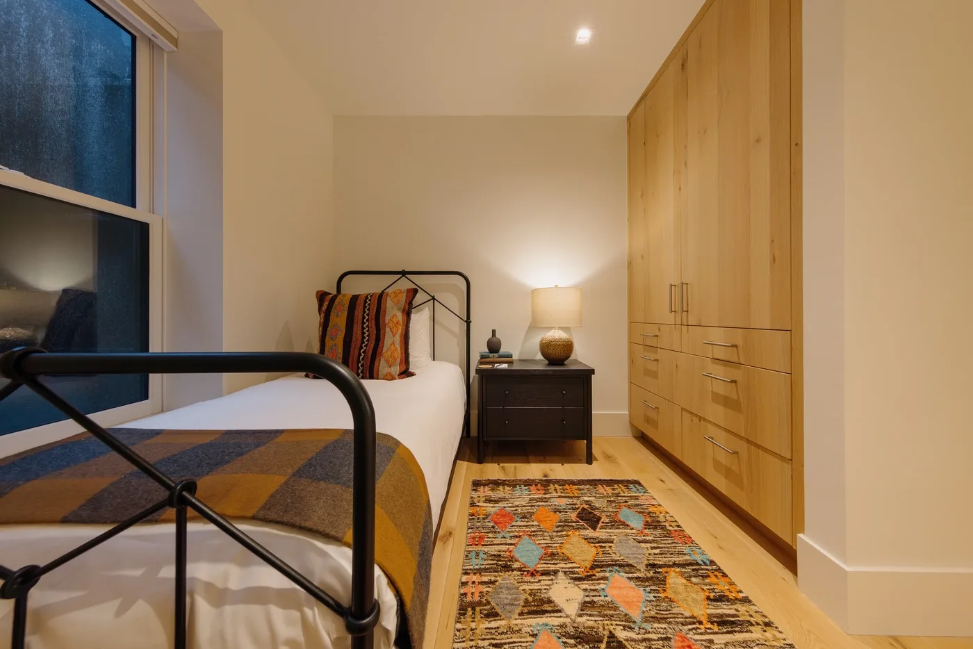 Un dormitorio con una cama individual, armarios de madera y una alfombra estampada.