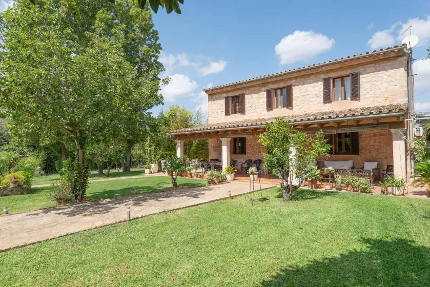 Una casa de dos plantas con un patio cubierto se alza junto a un césped verde.