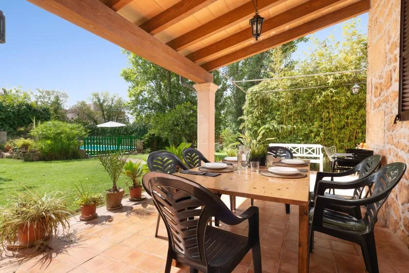 Comedor exterior cubierto con una mesa y sillas junto a un jardín.