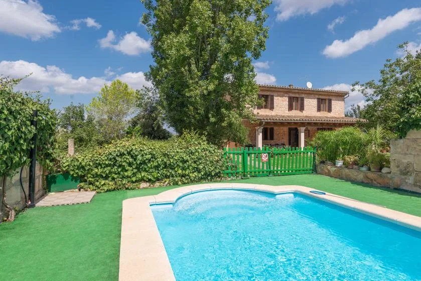 Una piscina está junto a un jardín frondoso y una casa de dos plantas.