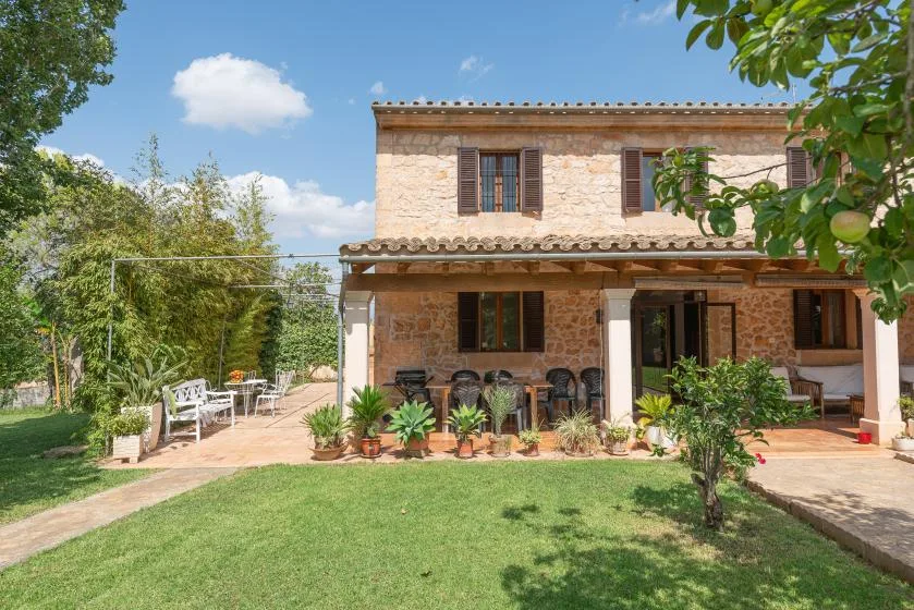 Una casa de piedra da a un patio ajardinado con asientos al aire libre y plantas en macetas.