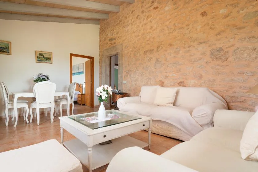 Una sala de estar con asientos claros junto a una pared de piedra y un comedor.