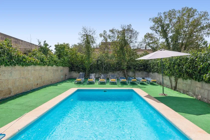 Una piscina está rodeada de césped artificial, tumbonas y una sombrilla.