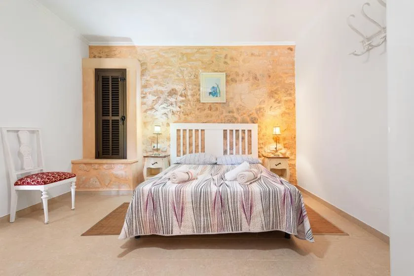 Dormitorio con una cama centrada frente a una pared de tonos cálidos y textura.