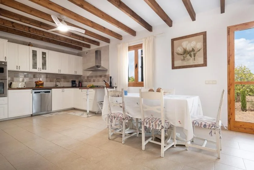 Una luminosa cocina y comedor con gabinetes blancos y una mesa bajo vigas expuestas.