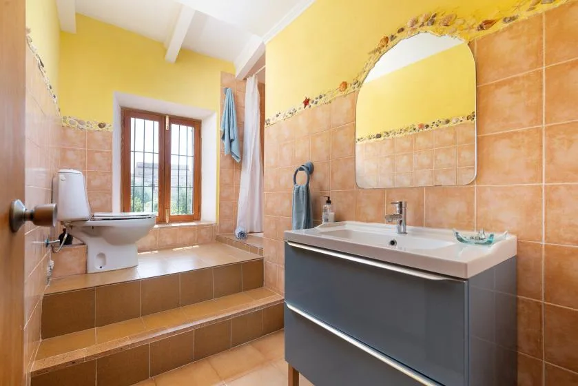 Un baño con azulejos, lavabo y váter junto a una ventana.
