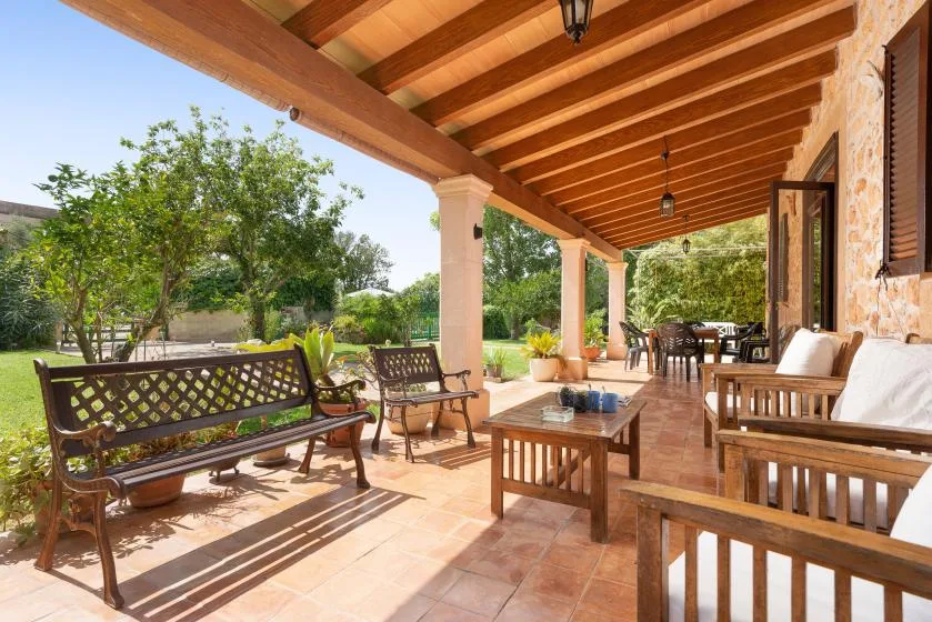 Un patio cubierto con asientos de madera y una mesa de comedor da a un jardín frondoso.