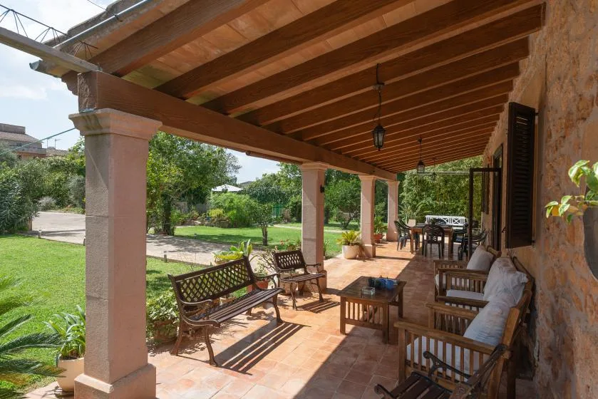 Un patio cubierto con asientos de madera da a un jardín verde.