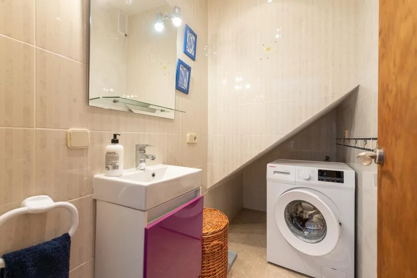 Un baño alicatado con lavabo, lavadora y cesta de mimbre.