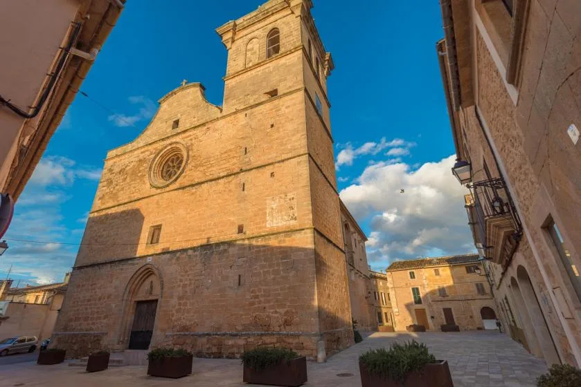 Una torre de iglesia de piedra se alza sobre una plaza pavimentada entre edificios antiguos.