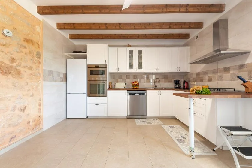 Una cocina luminosa con armarios blancos, electrodomésticos de acero inoxidable y vigas expuestas.