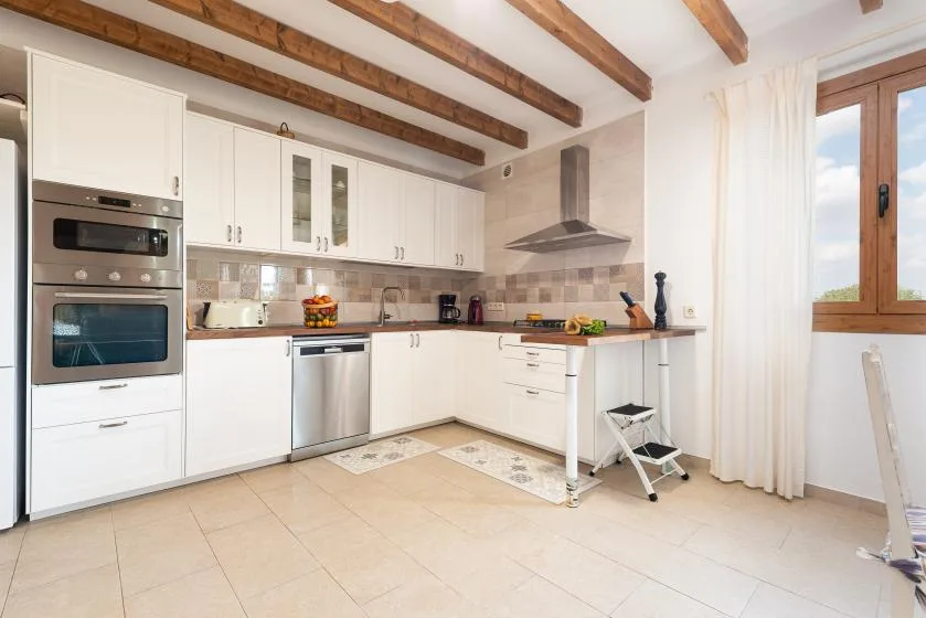 Una cocina luminosa con gabinetes blancos, electrodomésticos de acero inoxidable y vigas de madera vistas.
