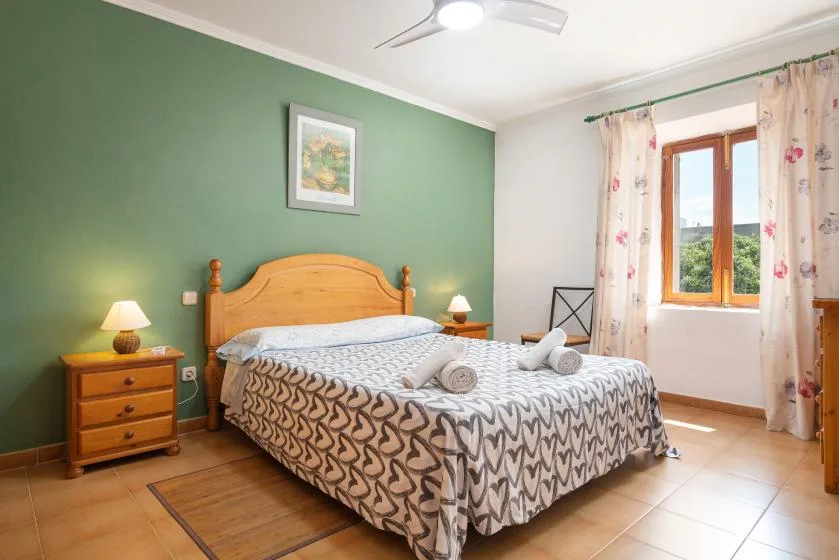 Un dormitorio con una cama doble, mesitas de madera y una ventana con cortinas florales.