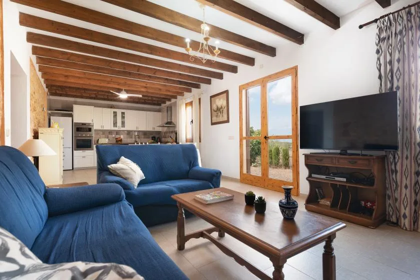 Una sala de estar con asientos azules, una mesa de centro y una cocina al fondo.