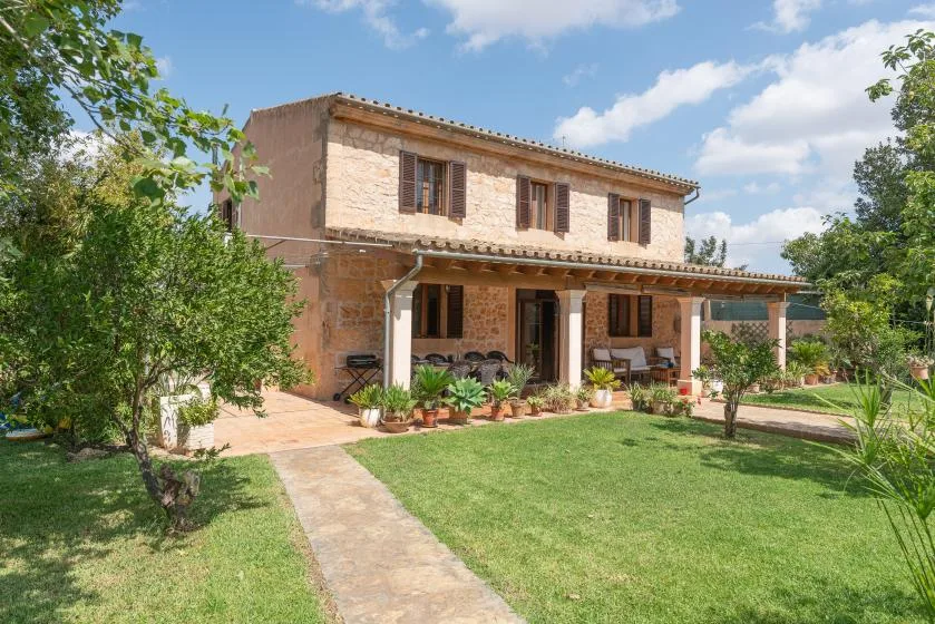 Una casa de dos plantas con patio cubierto da a un césped verde.