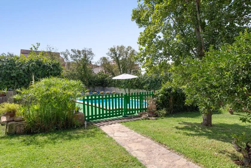 Un sendero del jardín conduce a una puerta verde junto a una piscina.