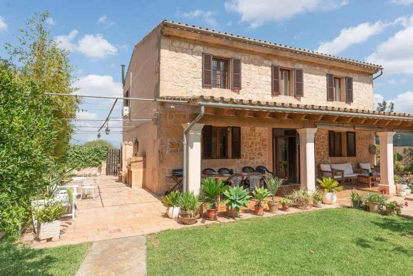 Una casa de piedra con patio cubierto, asientos al aire libre, plantas en macetas y césped.