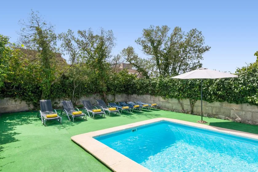 Una piscina al aire libre con asientos reclinables y una sombrilla.