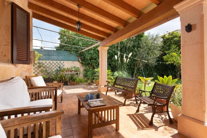 Un patio cubierto con asientos de madera se abre a un jardín frondoso.