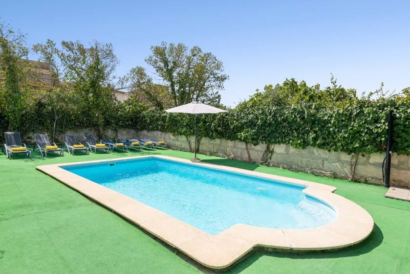 Una piscina al aire libre con asientos reclinables y una sombrilla al lado.