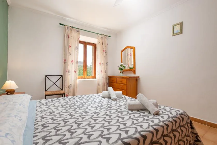 Un dormitorio con una colcha estampada, una cómoda de madera y una ventana.