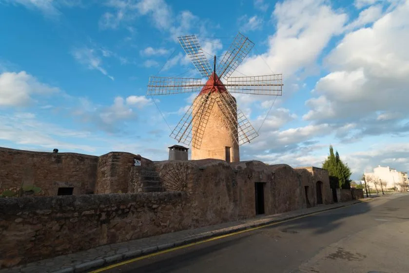 Un molino de piedra se eleva sobre un muro bajo junto a una carretera.