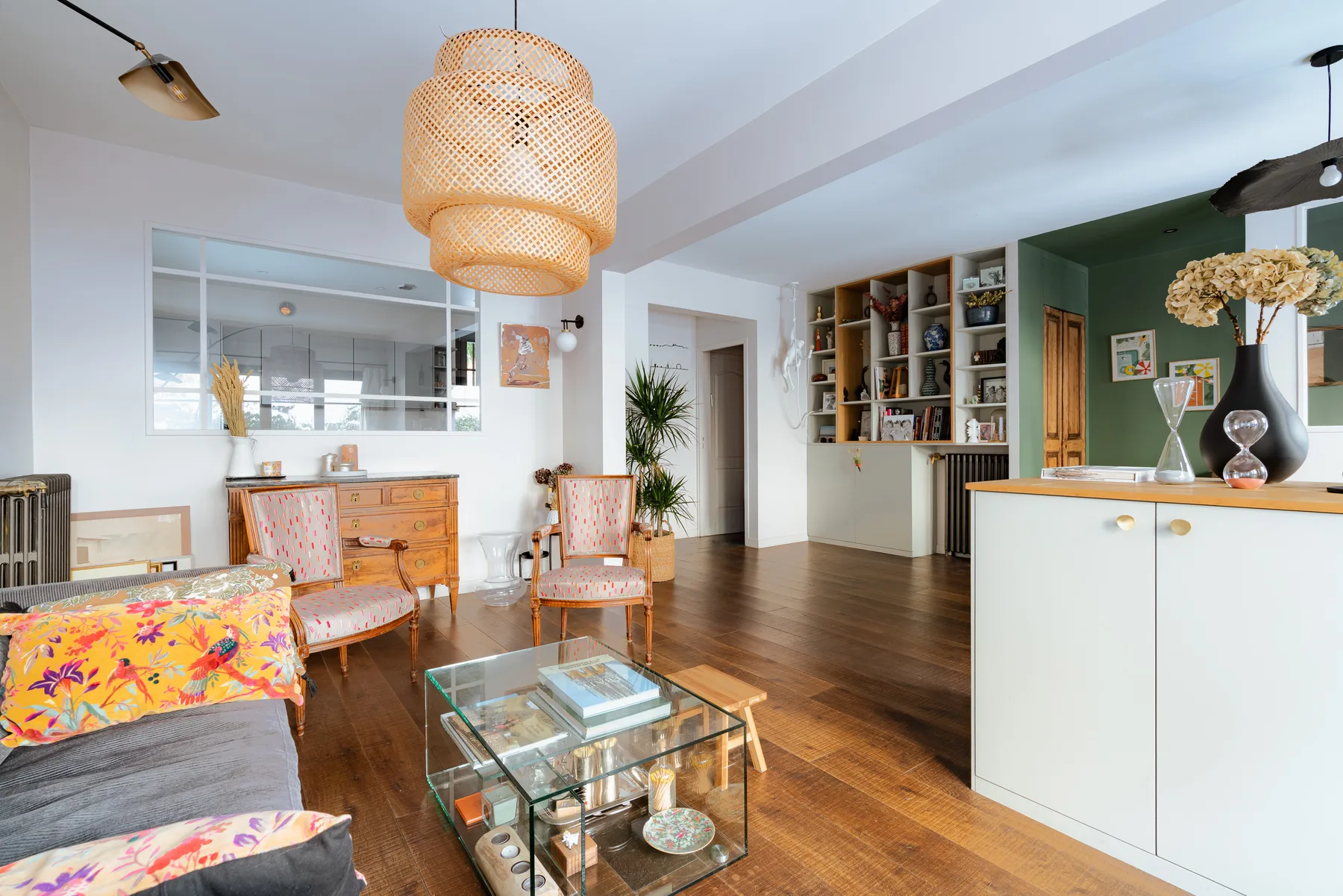 A bright living room with seating, a glass coffee table, and an open kitchen.