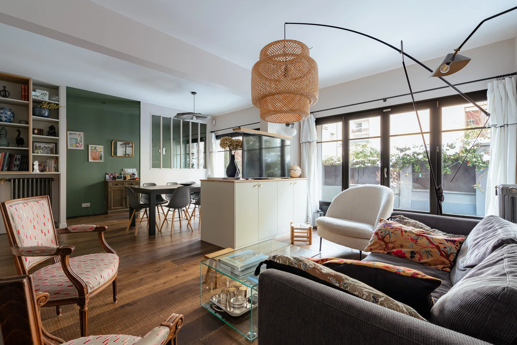 A bright living room opens onto a dining area and a row of large windows.