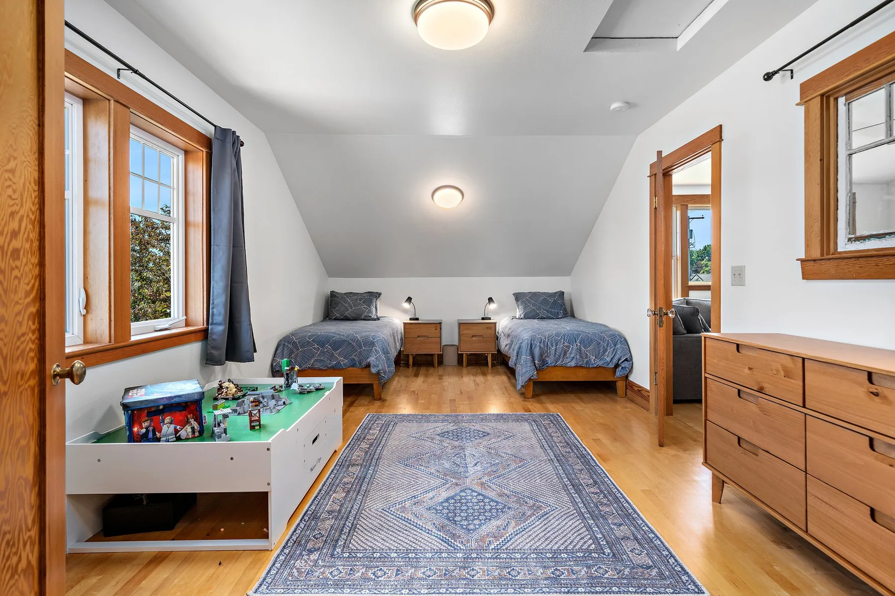 Un dormitorio luminoso con dos camas, una alfombra y muebles de madera.
