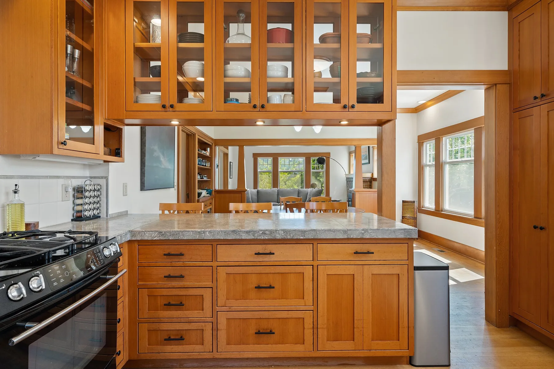 Cocina con gabinetes de madera, una isla central y ventanas hacia un comedor.