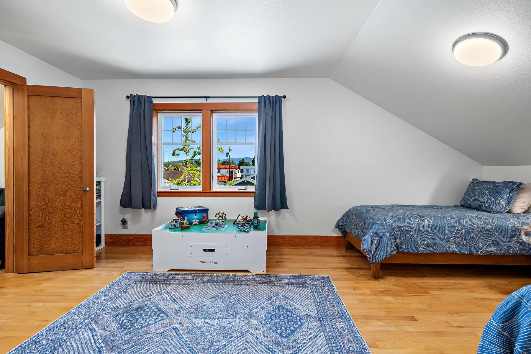 Un dormitorio luminoso con una cama, una ventana y una alfombra azul estampada.