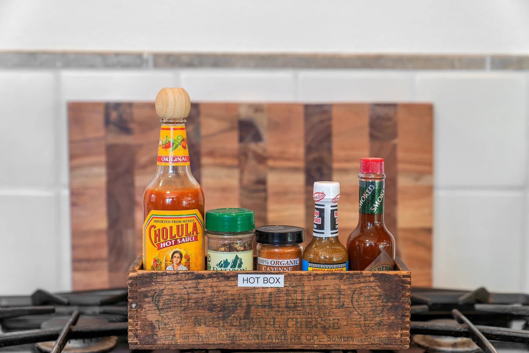 Una caja de madera con varias botellas de condimentos está sobre una estufa de gas.