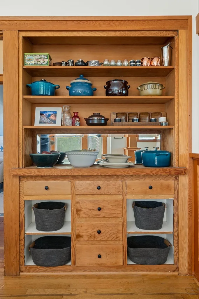 Un aparador de cocina de madera exhibe utensilios de cocina, vajilla y cestas.