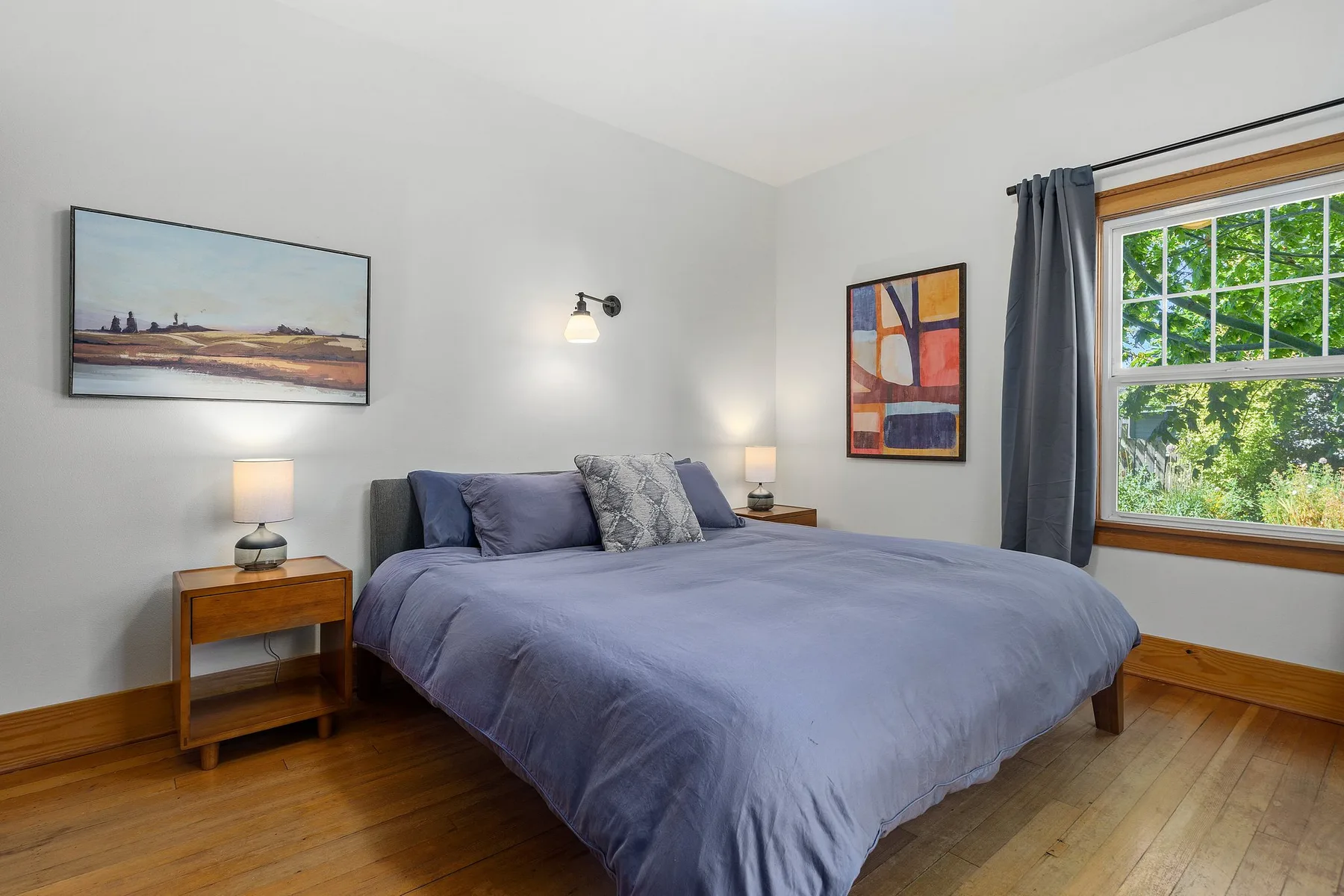 Un dormitorio con una cama, cuadros enmarcados y una ventana con cortinas.